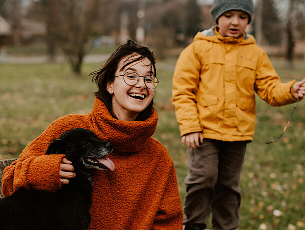 Mutter sitzt mit Sohn und Hund lachend auf einem Baumstamm Mutter sitzt mit Sohn und Hund lachend auf einem Baumstamm