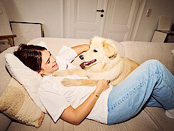 Frau liegt kuschelnd mit Hund auf der Couch