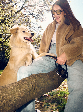 Frauchen sitzt mit ihrem Hund auf einem Baumstamm und lacht